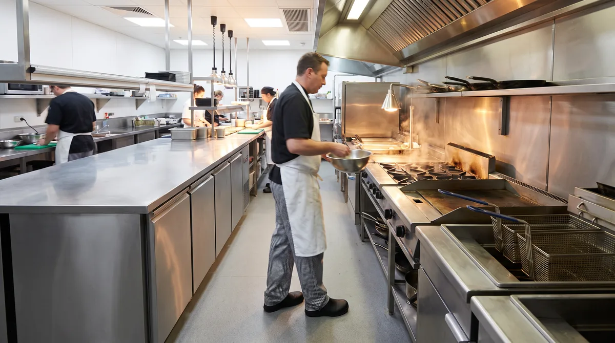 An underbench refrigerator installed directly beside a hot cooking line, with a chef moving between the two.